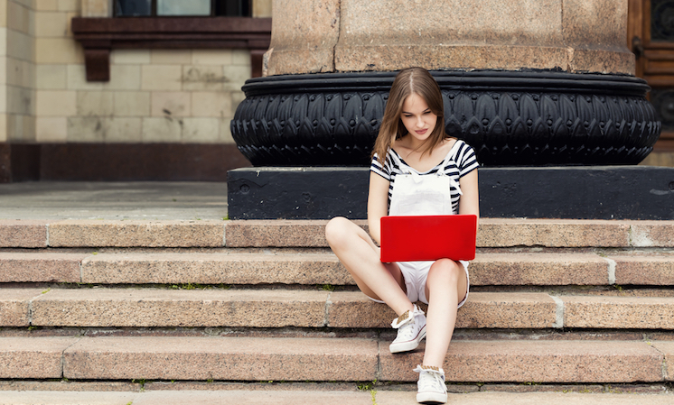 Young woman with laptop sitting on stairs near the university