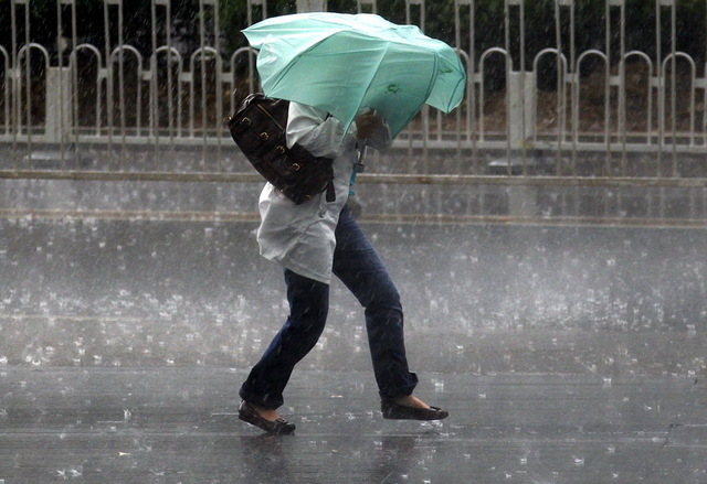 A woman struggles to hold an umbrella as she walks through a storm in Beijing